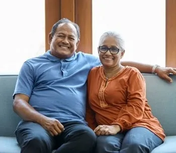 A couple sitting on the couch, leaning on each other and smiling.