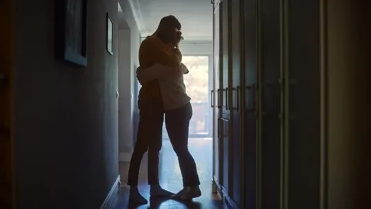 A man and a woman hugging tightly against the light outside the room.