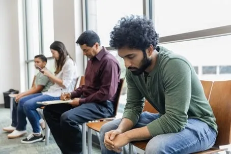 Four people sitting, and a man in front who looks tired and troubled.